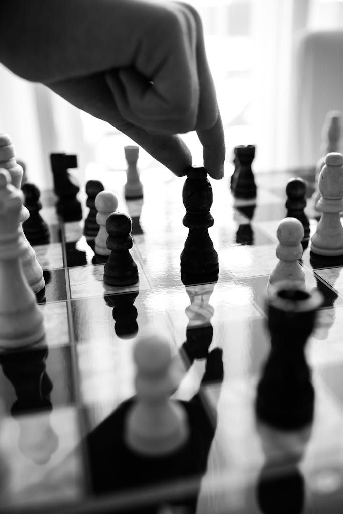 Black and white close-up of chess game with strategic move, hand placing piece.